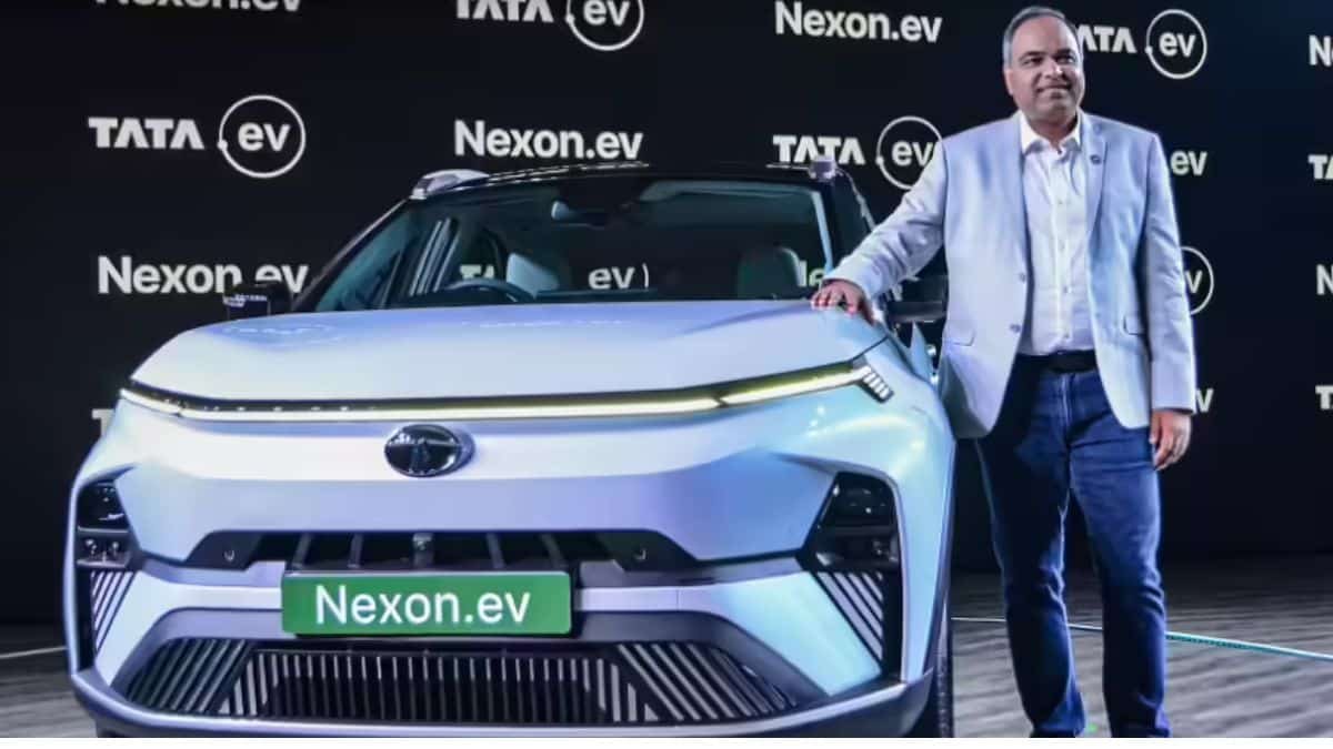 Shailesh Chandra speaking about entry-level electric vehicles in India with Tata electric cars and EV charging infrastructure in the background.