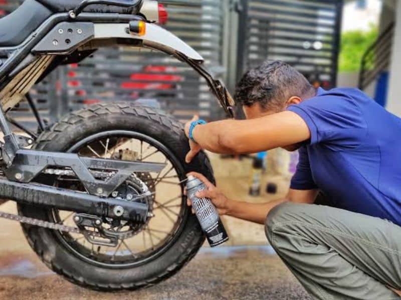 A mechanic lubricating a motorcycle drive chain during routine maintenance